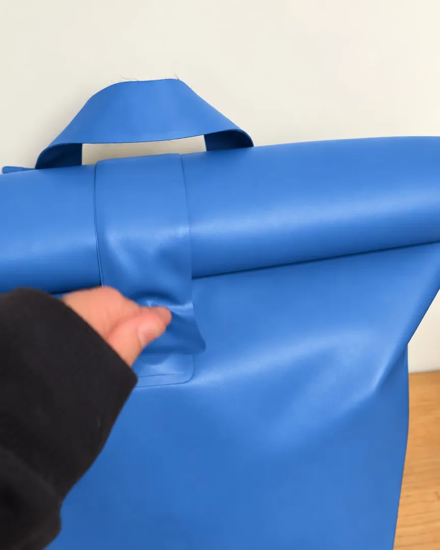 A child's hands closing the flat central tab on a plop roll-top bag